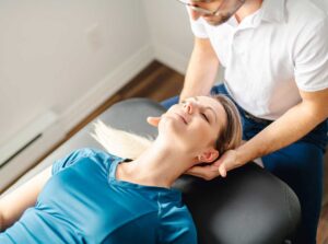A chiropractor assessing the posture of a young athlete in a clinic setting with exercise equipment visible.